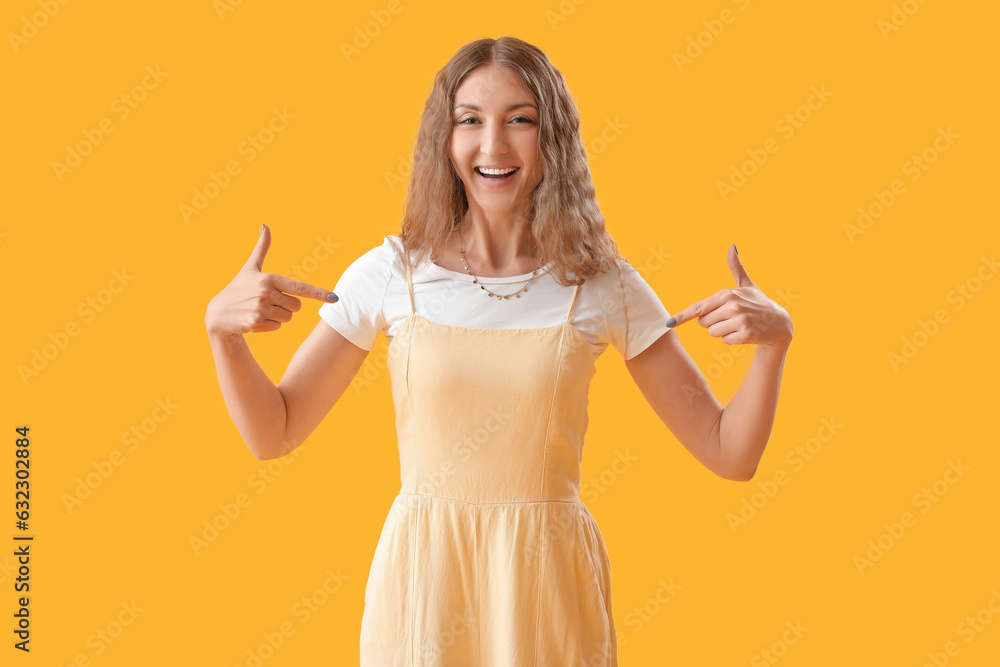 Beautiful young woman pointing at her dress on yellow background