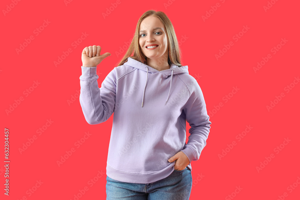 Beautiful redhead woman in hoodie pointing at herself on red background