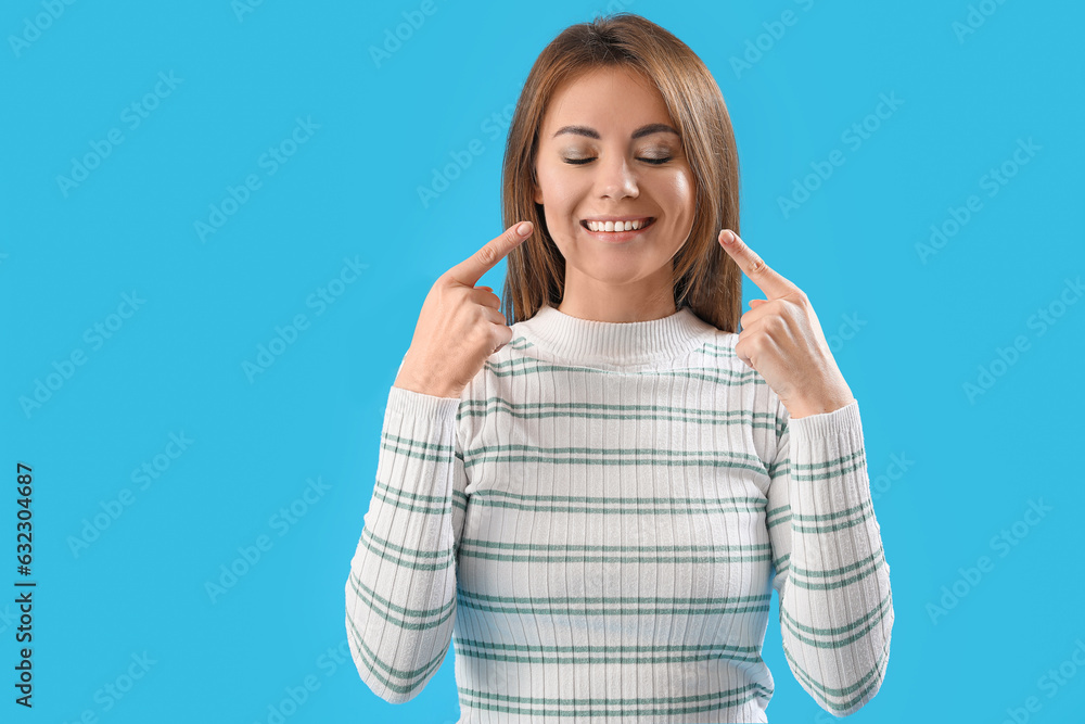 Beautiful woman pointing at her smile on blue background