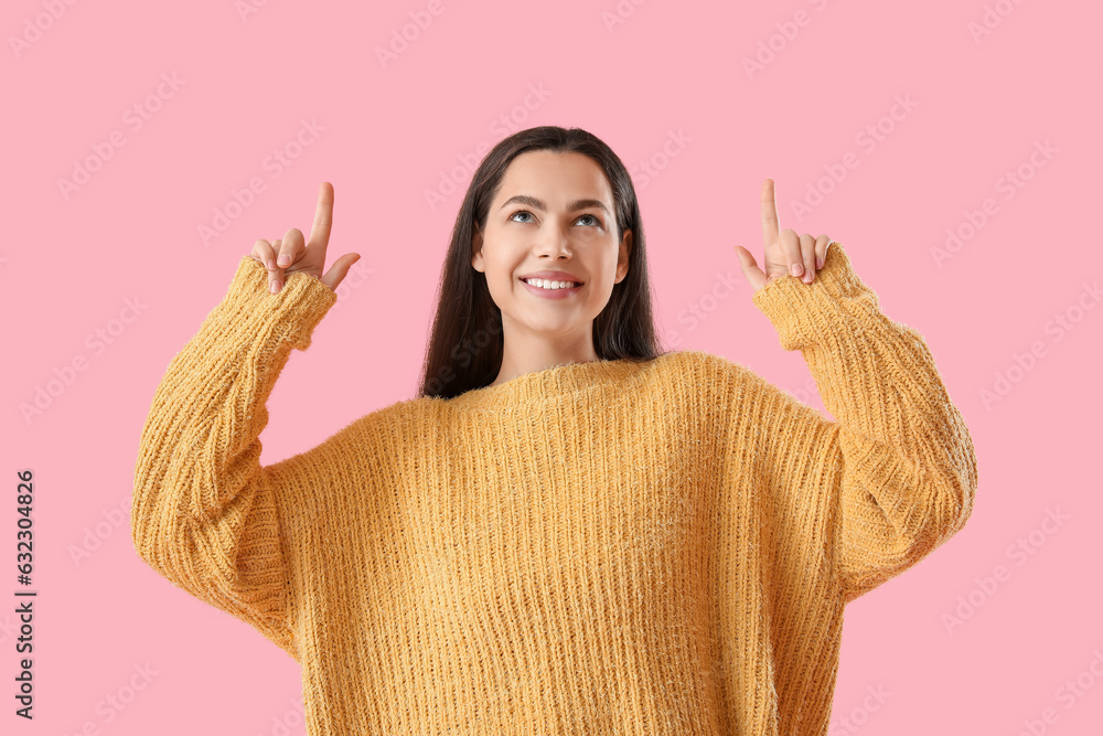 Beautiful young woman pointing at something on pink background