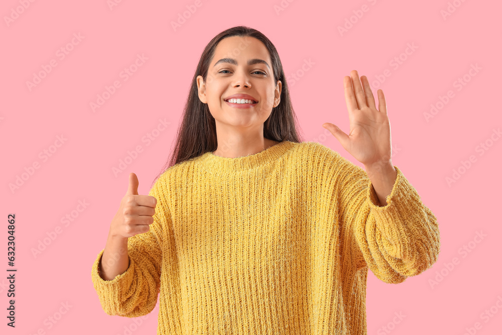 Beautiful young woman showing thumb-up on pink background