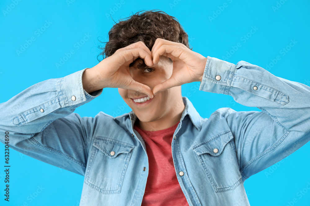 Handsome young man making heart with his hands on light blue background