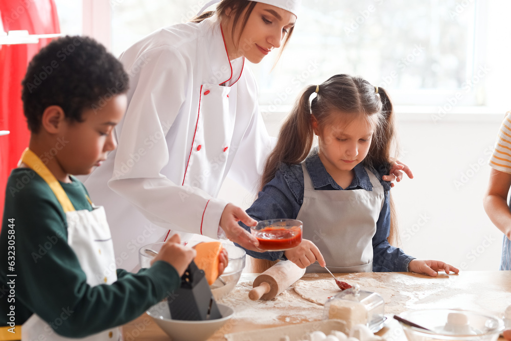 Female chef with group of little children preparing pizza during cooking class in kitchen