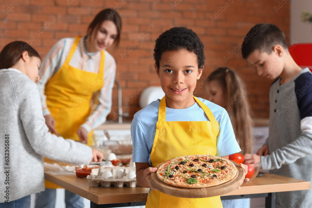 Little African-American boy with prepared pizza after cooking class in kitchen