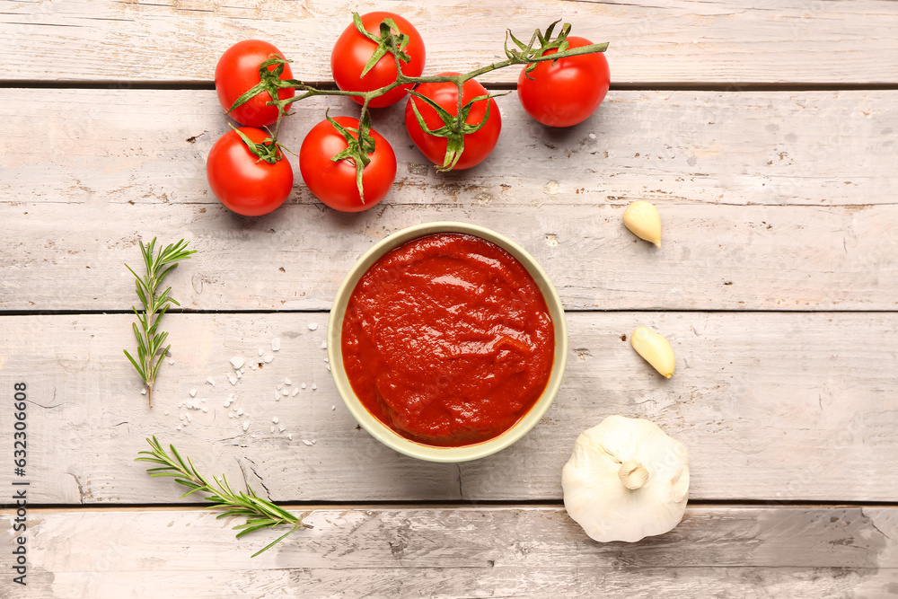 Bowl with tasty tomato paste and fresh vegetables on light wooden background