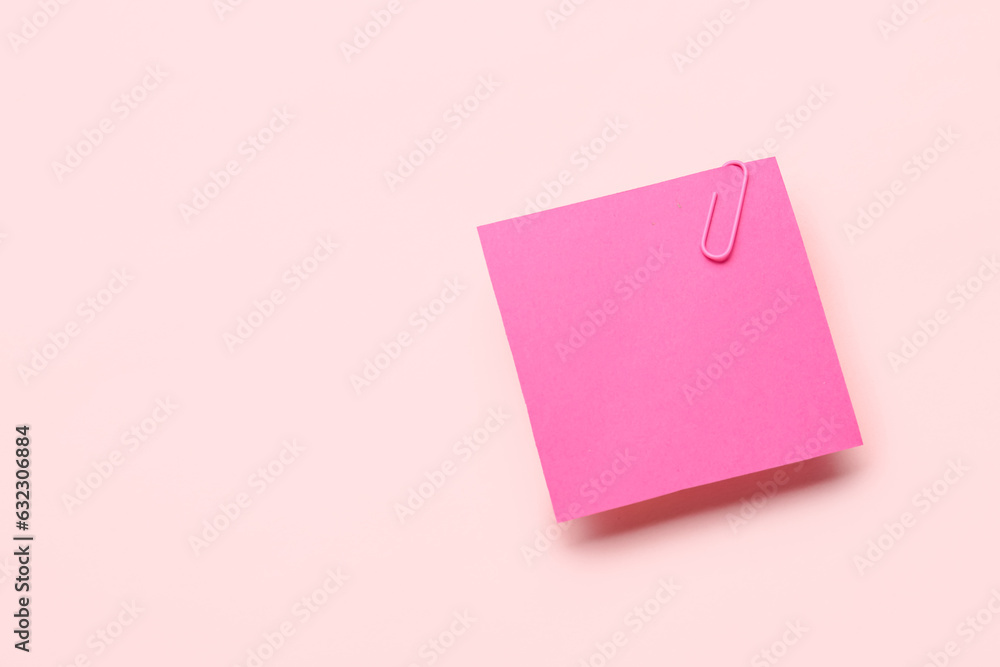 Pink sticky note with paper clip on color background