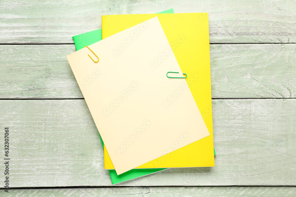 Beige, yellow and green paper sheets with clip on color wooden background