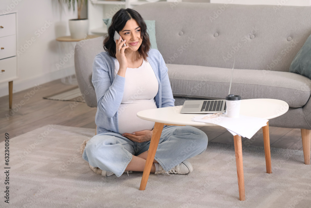 Working pregnant woman talking by mobile phone at home