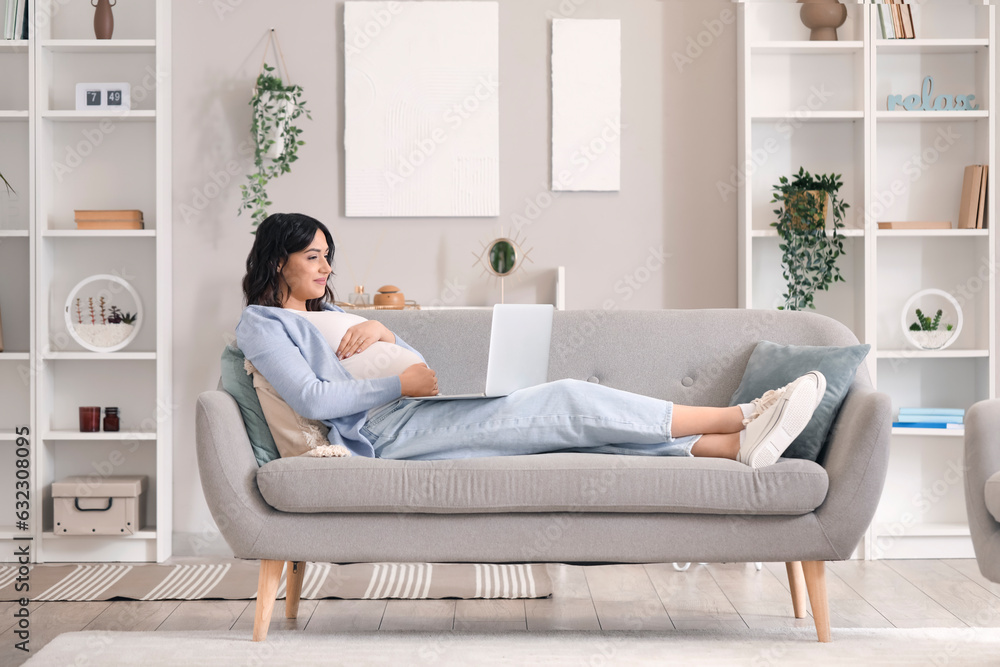 Young pregnant woman working with laptop on sofa at home