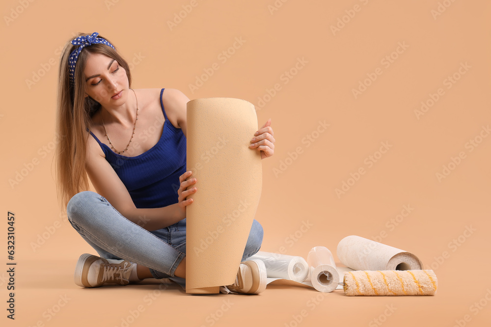 Young woman with wallpaper roll sitting on beige background