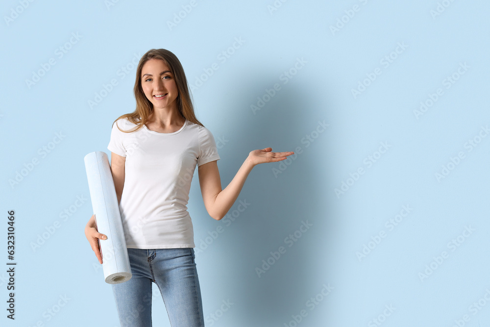 Young woman with wallpaper roll showing something near blue wall