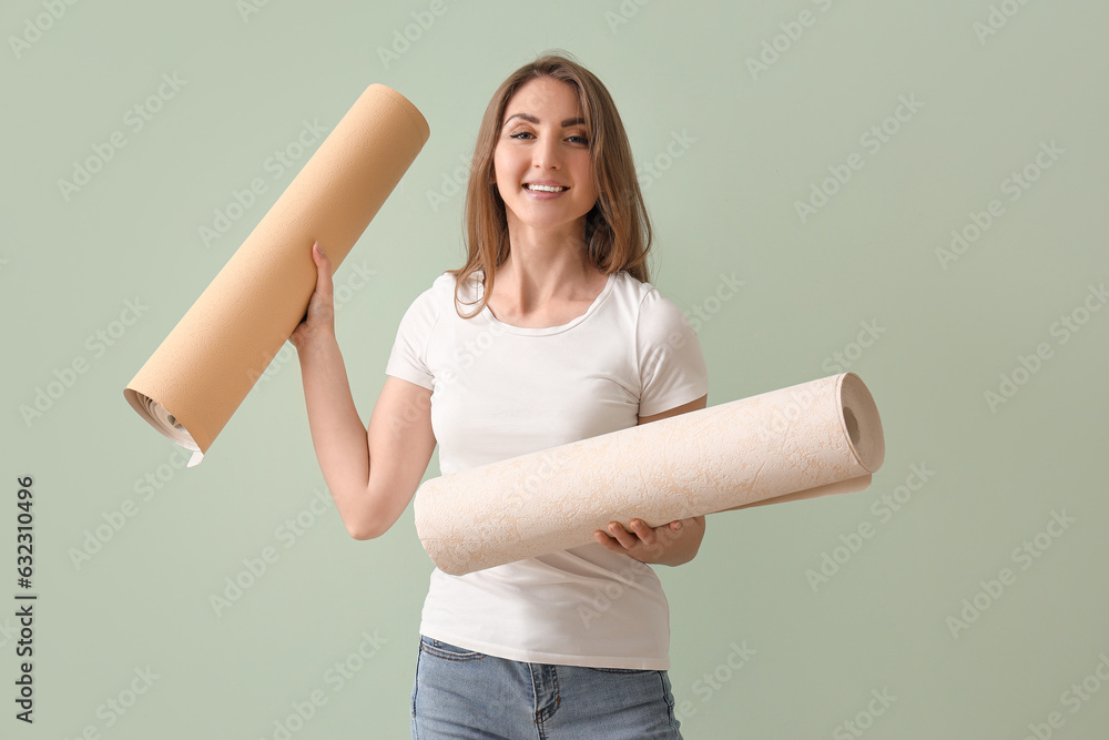 Young woman with wallpaper rolls on green background