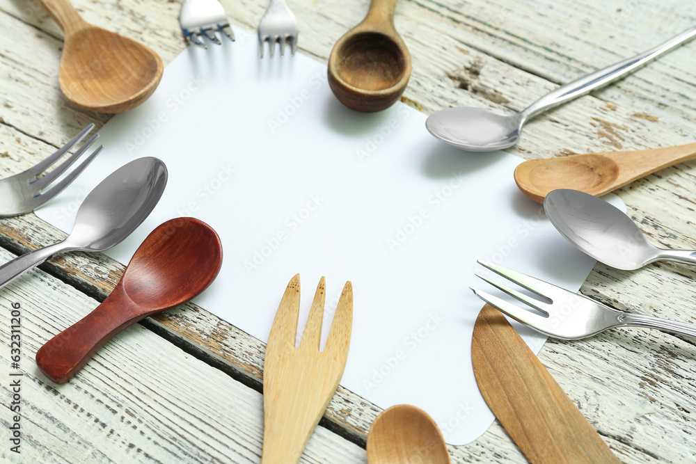 Frame made of blank card and different cutlery on light wooden background, closeup