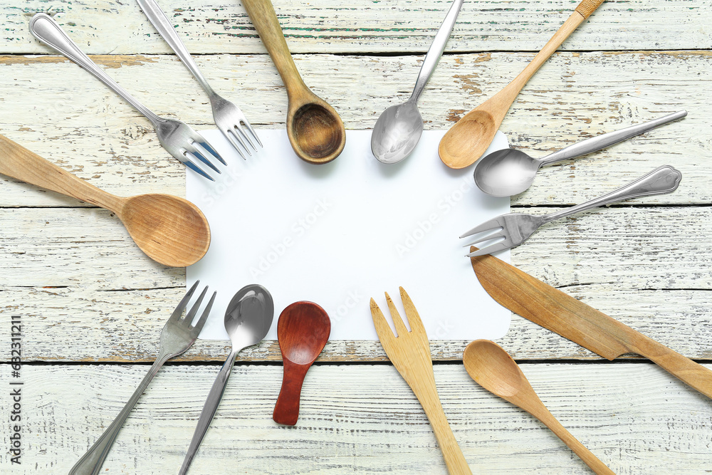 Frame made of blank card and different cutlery on light wooden background