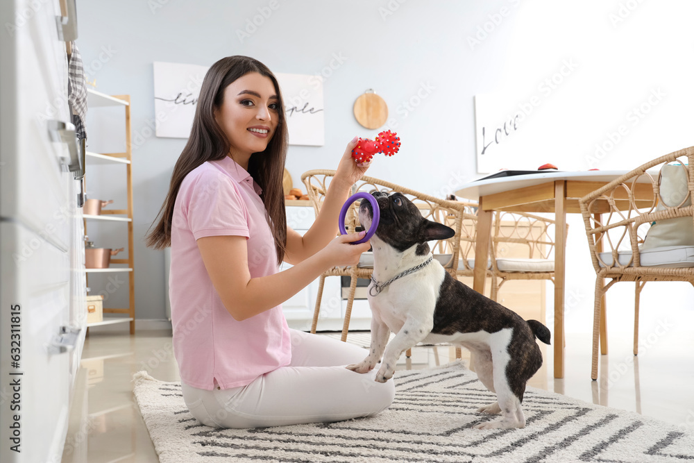 Young woman playing with her French bulldog in kitchen