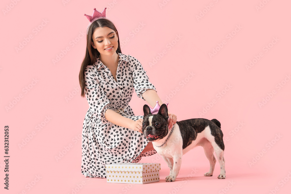 Young woman with her French bulldog and crowns on pink background