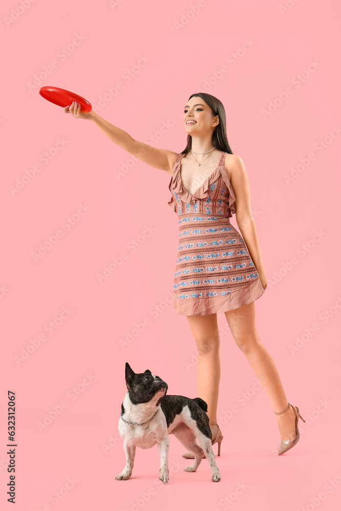 Young woman with frisbee disk and her French bulldog on pink background