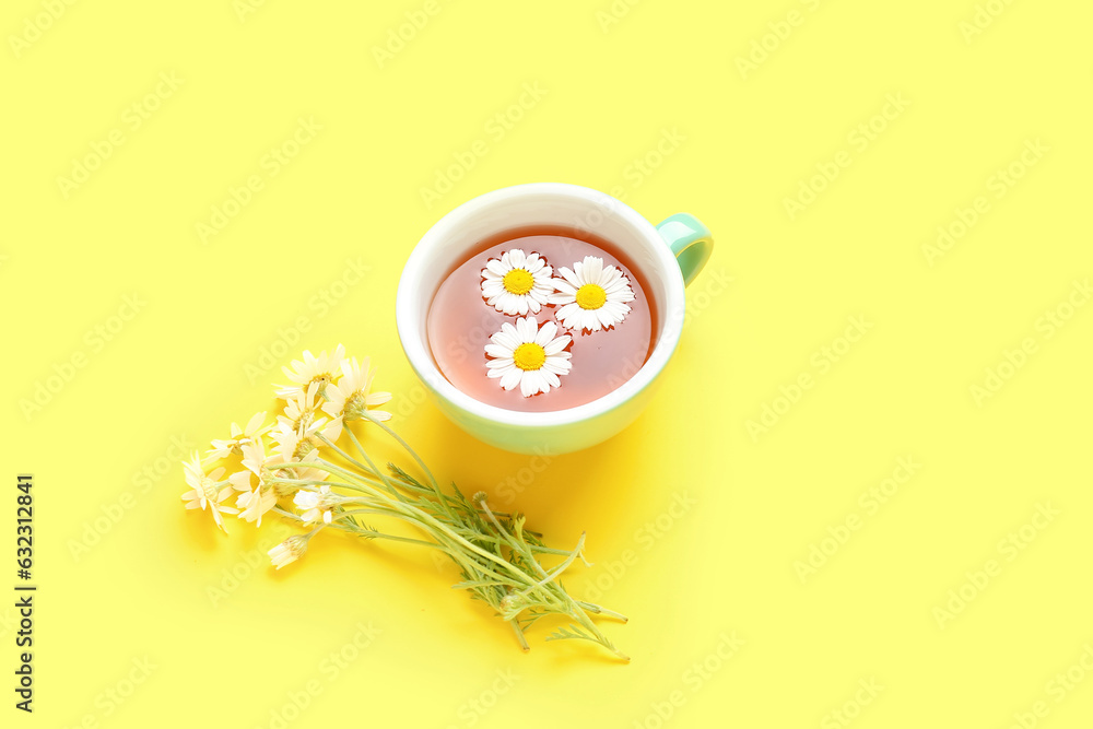 Cup of natural chamomile tea and flowers on yellow background