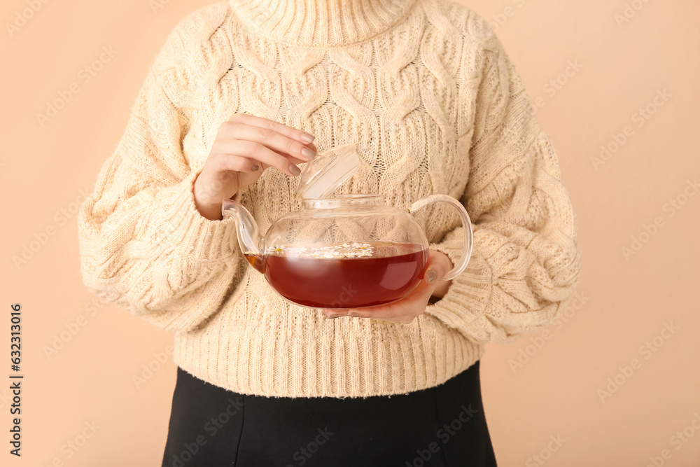 Beautiful young woman with teapot of chamomile tea near beige wall