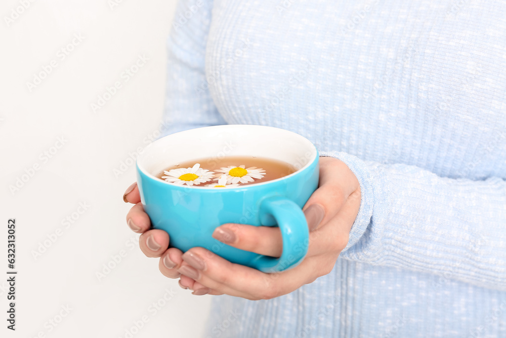 Beautiful young woman with cup of chamomile tea near white wall