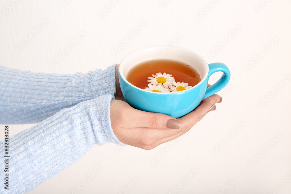 Female hands with cup of chamomile tea near white wall