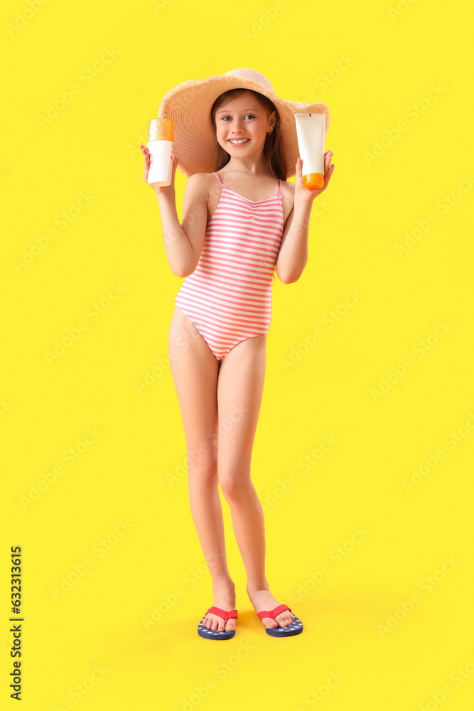 Little girl with bottles of sunscreen cream on yellow background