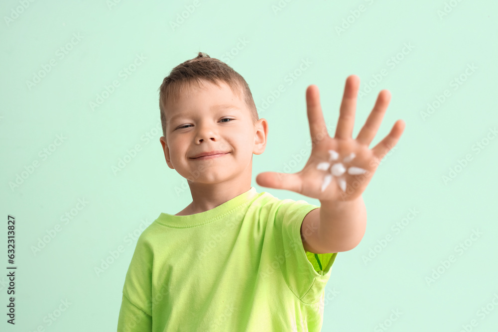 Little boy showing palm with sunscreen cream on pale green background