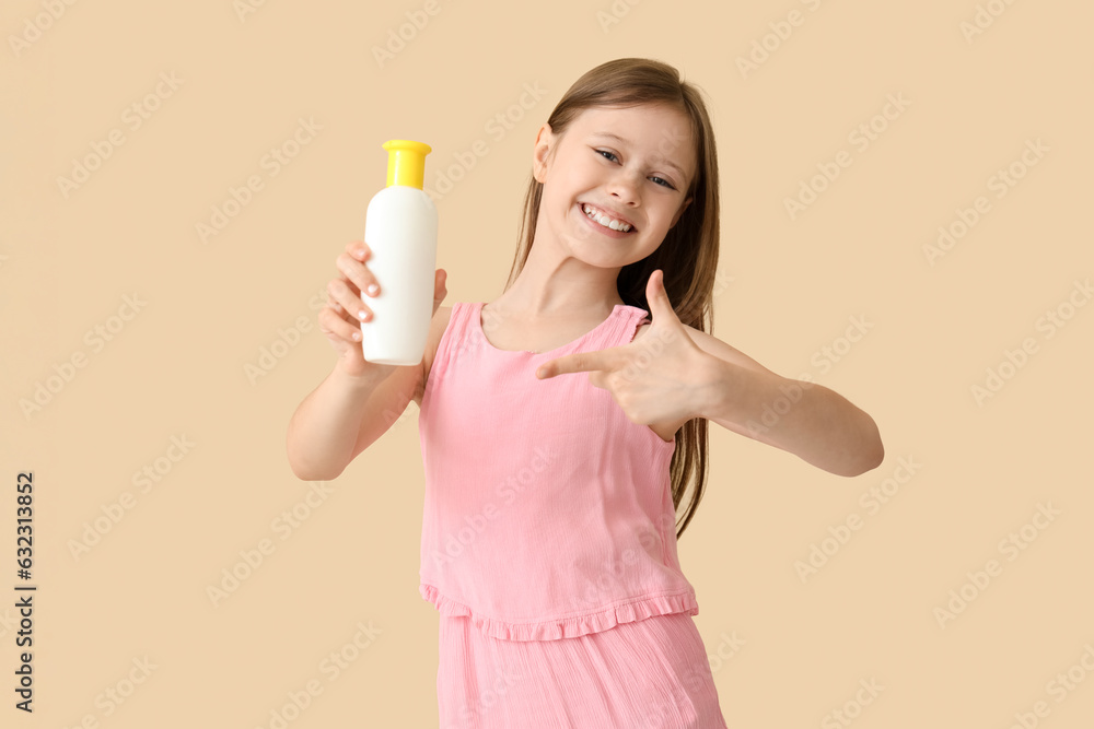 Little girl pointing at bottle of sunscreen cream on beige background