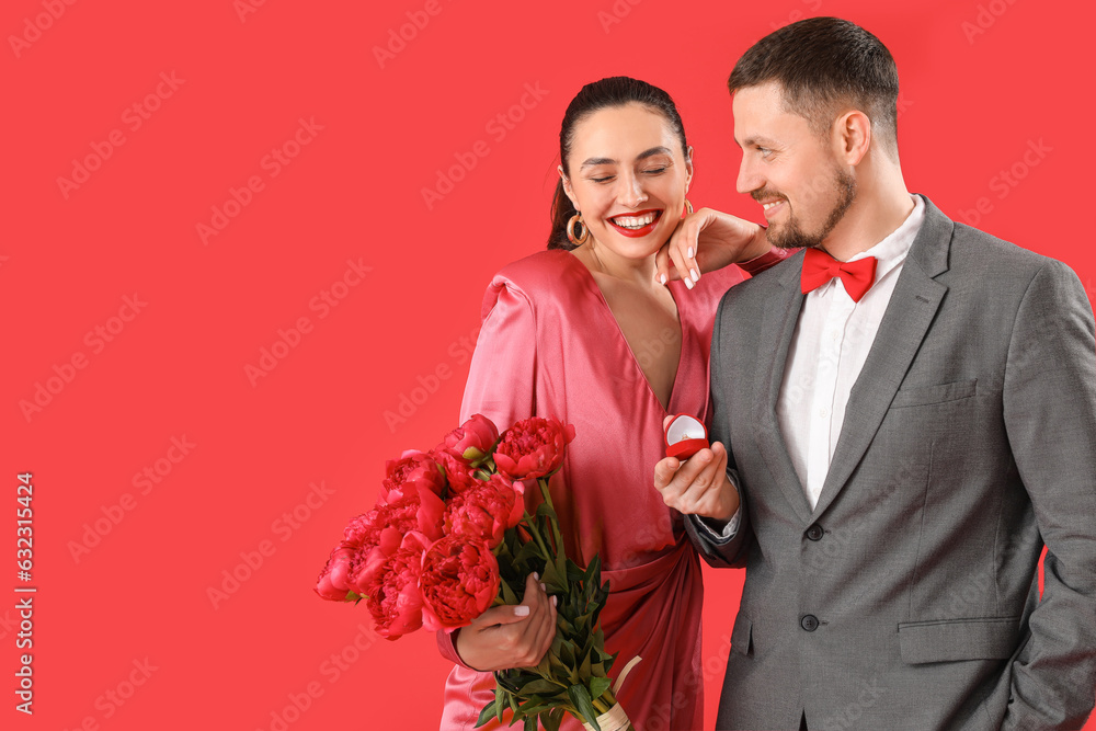 Young man proposing to his girlfriend with flowers on red background