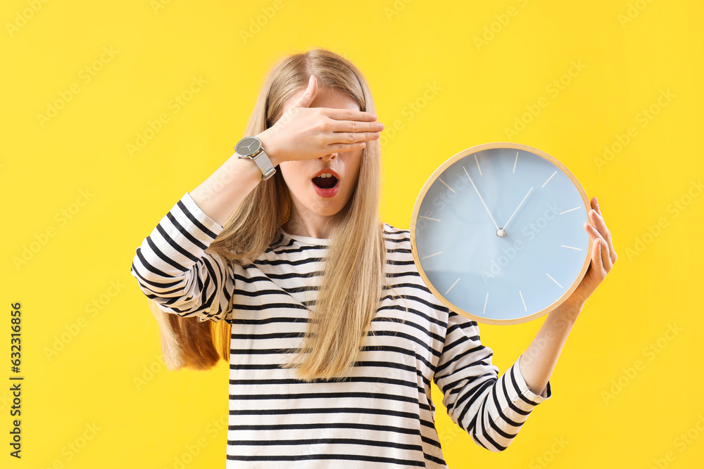 Stressed young woman with clock on yellow background. Deadline concept