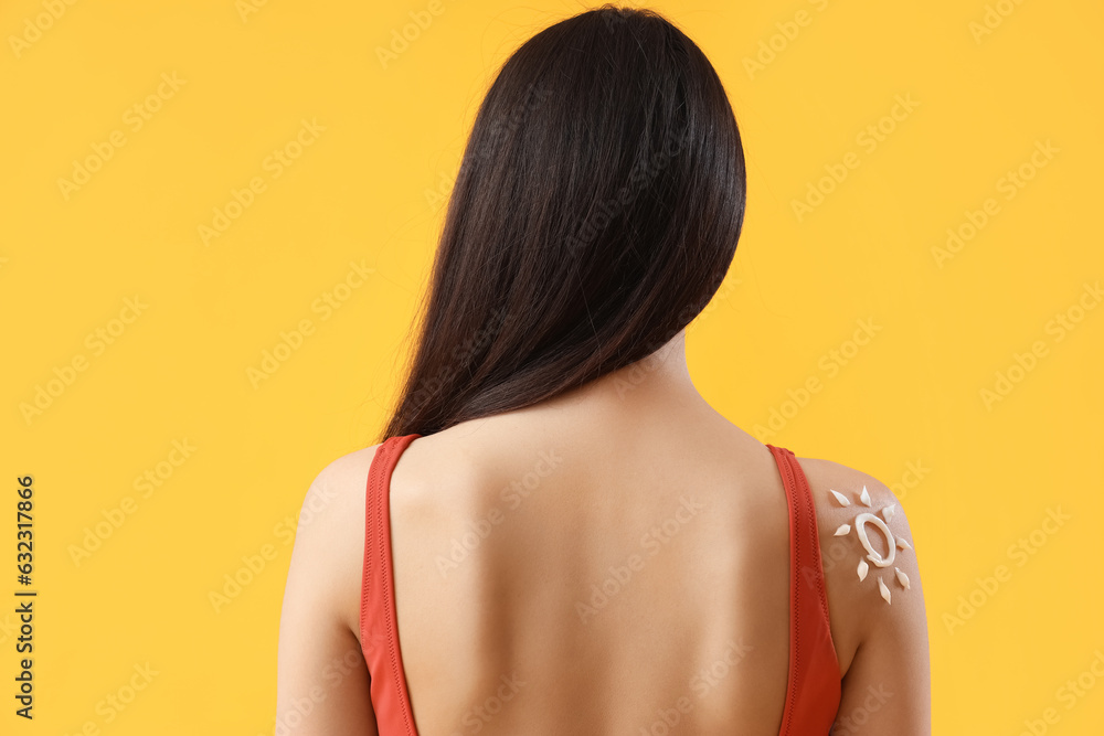 Young woman with sun made of sunscreen cream on her shoulder against yellow background, back view