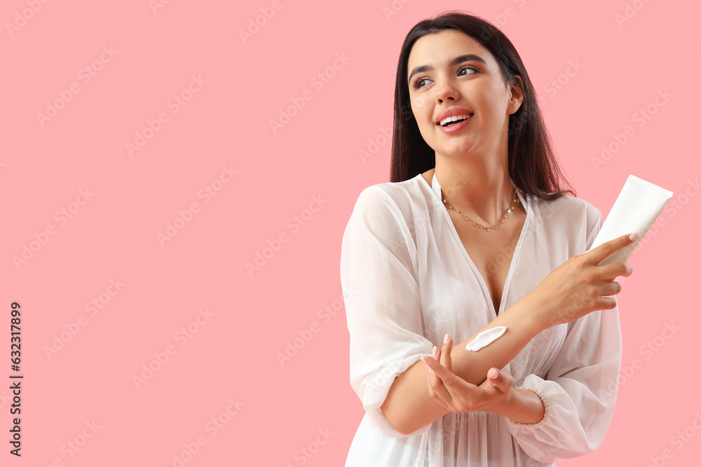 Young woman applying sunscreen cream on pink background