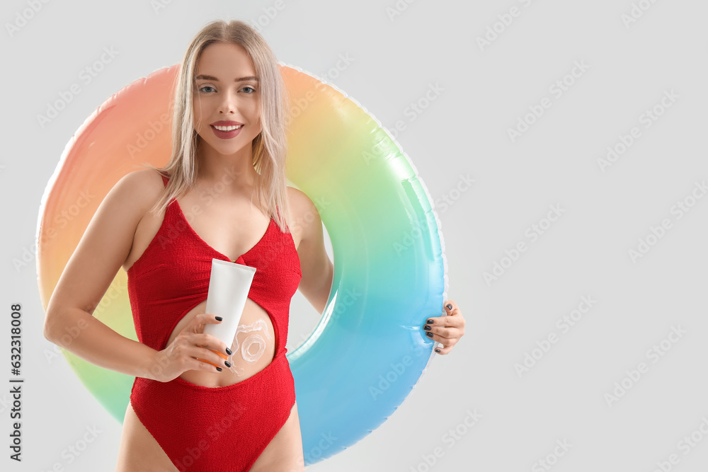 Young woman with sunscreen cream and inflatable ring on light background