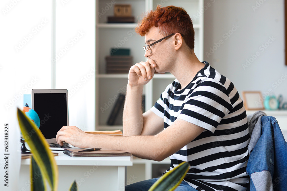 Young redhead man studying with laptop at home