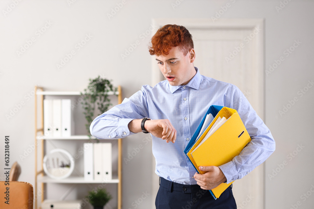 Shocked redhead businessman with folders looking at wristwatch in office