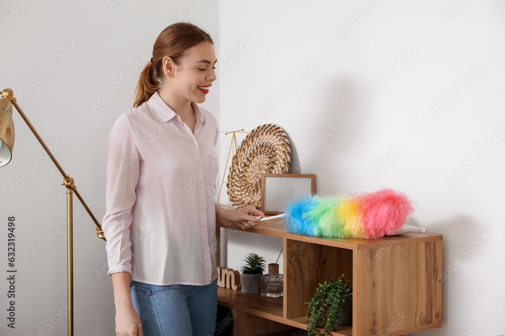 Young woman cleaning shelf with pp-duster at home