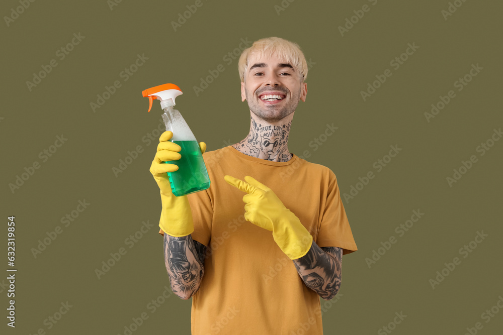 Young tattooed man pointing at spray bottle of detergent on green background