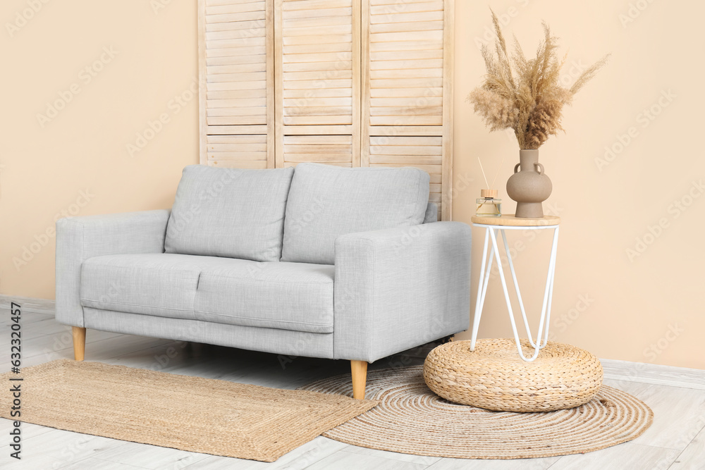 Stylish grey sofa, folding screen, table and pampas grass near beige wall in room