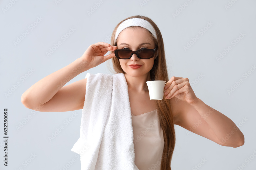 Pretty young woman in pajamas, with towel and coffee on light background