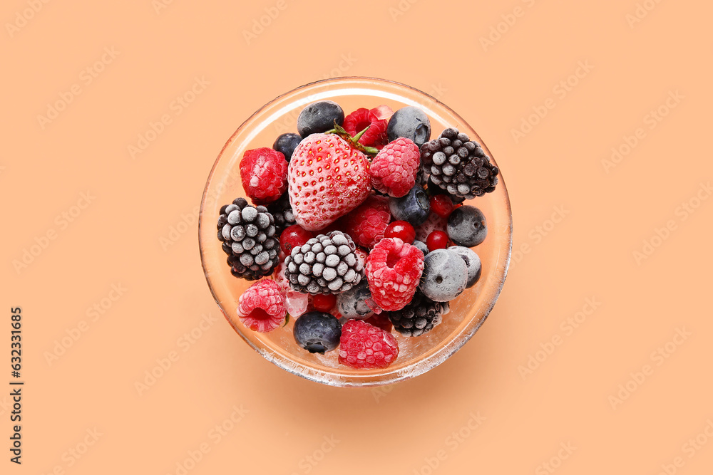 Glass bowl of frozen berries on color background