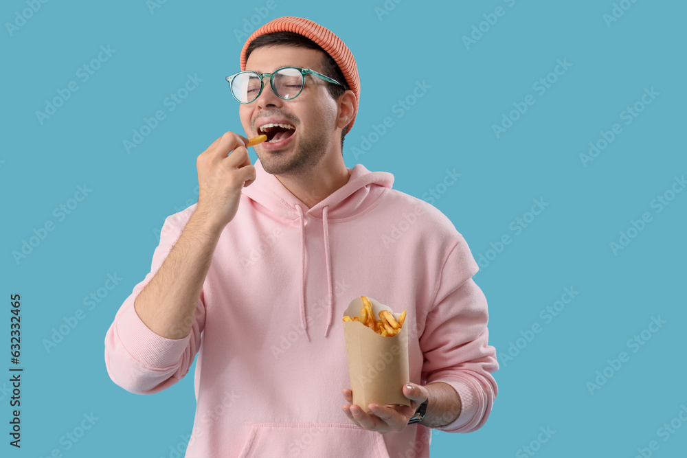 Young man eating french fries on blue background