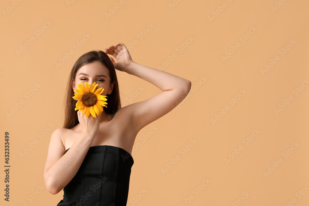 Young woman with beautiful sunflower on orange background