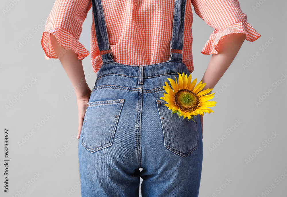 Young woman with beautiful sunflower on grey background, back view