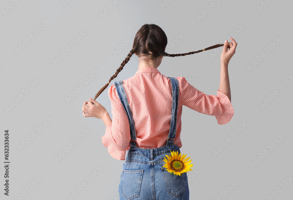 Young woman with beautiful sunflower on grey background, back view