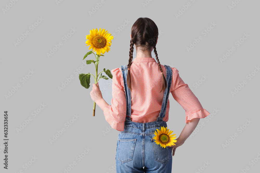 Young woman with beautiful sunflowers on grey background, back view