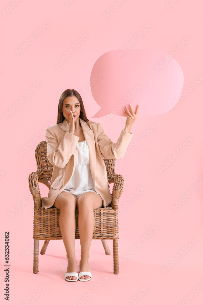 Beautiful young woman with speech bubble sitting on wicker chair against pink background