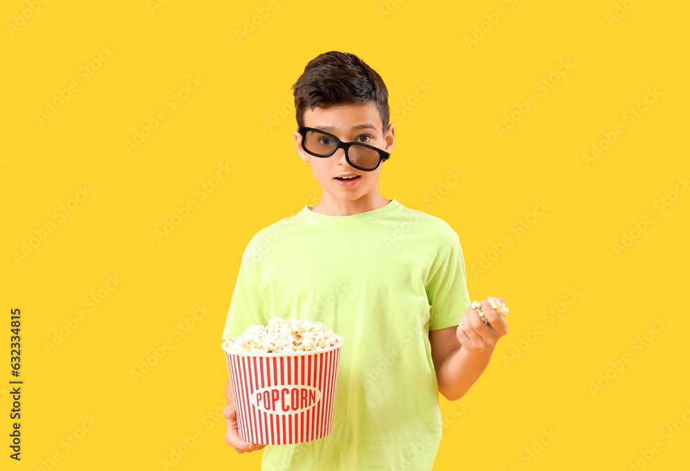 Shocked little boy in 3D glasses with popcorn on orange background