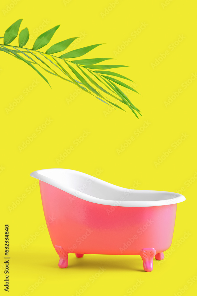 Small bathtub and palm leaf on yellow background