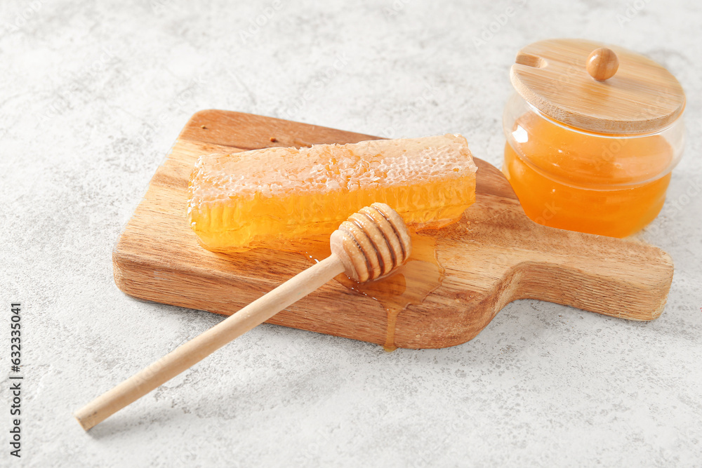 Jar of sweet honey, comb and dipper on light background