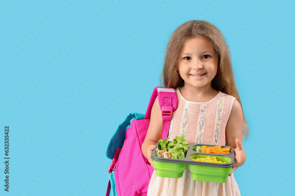 Happy little girl with backpack and lunchbox on blue background